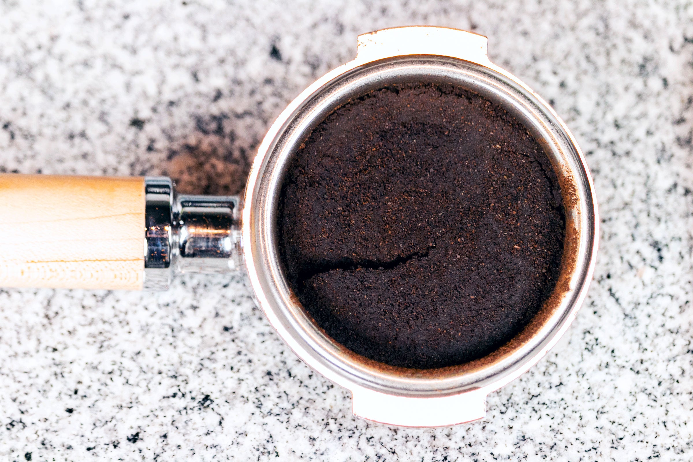 A cracked espresso puck inside a maple portafilter